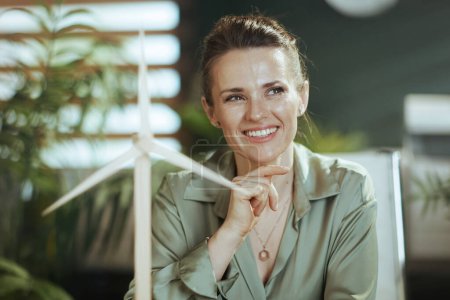 Foto de Feliz joven dueño de la pequeña empresa mujer en blusa verde en moderna oficina verde con molino de viento - Imagen libre de derechos