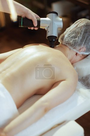 Photo for Healthcare time. massage therapist in spa salon with massage pistol massaging clients neck on massage table. - Royalty Free Image