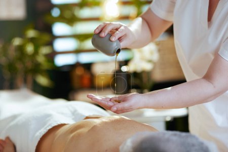 Foto de Tiempo de atención médica. Primer plano del masajista en el gabinete de masaje con el cliente usando aceite en la mesa de masaje. - Imagen libre de derechos