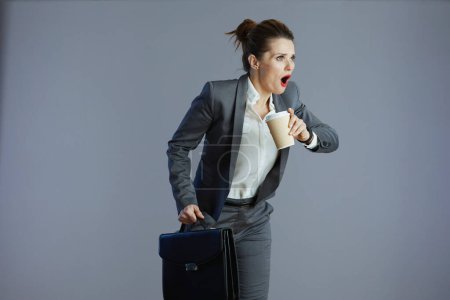 Photo for Fury stylish middle aged woman worker in grey suit with coffee cup and briefcase running isolated on grey. - Royalty Free Image