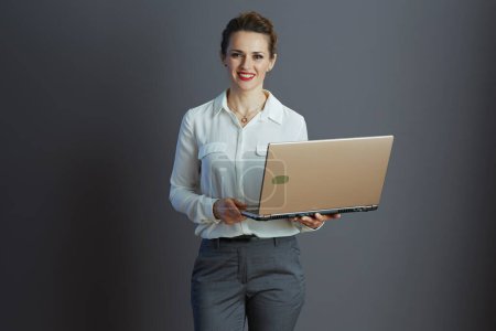 Téléchargez les photos : Heureux moderne 40 ans femme travailleur en chemisier blanc à l'aide d'un ordinateur portable isolé sur fond gris. - en image libre de droit