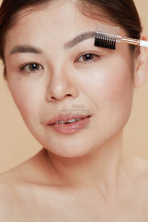 Téléchargez les photos : Moderne asiatique femelle avec brosse frontale sur fond beige. - en image libre de droit
