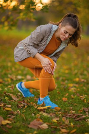 Foto de Hola otoño. triste mujer moderna en ropa de fitness en el parque tiene una lesión en la pierna. - Imagen libre de derechos
