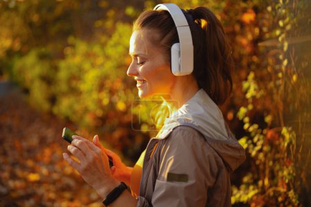 Foto de Hola otoño. mujer elegante sonriente en ropa de fitness en el parque escuchando la música con auriculares. - Imagen libre de derechos