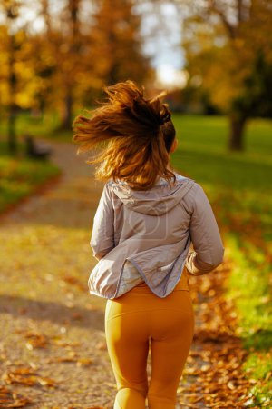 Photo for Hello autumn. Seen from behind modern woman in fitness clothes in the park jogging. - Royalty Free Image