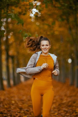Photo for Hello autumn. happy 40 years old woman in fitness clothes in the park running. - Royalty Free Image