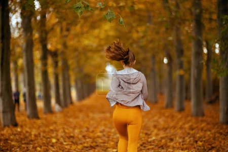 Foto de Hola otoño. Visto desde atrás elegante mujer en ropa de fitness en el parque corriendo. - Imagen libre de derechos