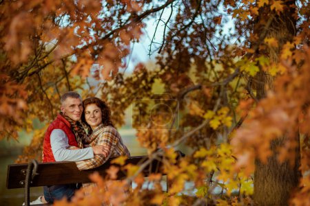 Foto de Hola otoño. feliz romántico novio y novia en el parque sentado en el banco. - Imagen libre de derechos