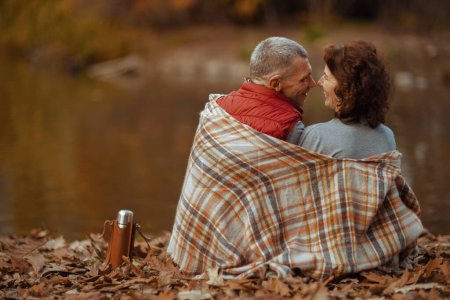 Foto de Hola otoño. Visto desde atrás pareja moderna en el parque con manta abrazo. - Imagen libre de derechos