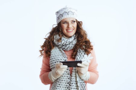 Foto de Hola invierno. feliz elegante 40 años de edad mujer en suéter, mitones, sombrero y bufanda contra fondo blanco con copo de nieve utilizando la aplicación de teléfono inteligente. - Imagen libre de derechos