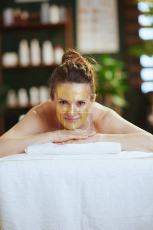 Téléchargez les photos : Temps de santé. femme moderne détendue dans le salon de spa avec masque cosmétique doré sur la pose du visage sur la table de massage. - en image libre de droit