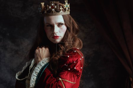 Foto de Pensativa reina medieval en vestido rojo con maquillaje blanco y corona sobre fondo gris oscuro. - Imagen libre de derechos