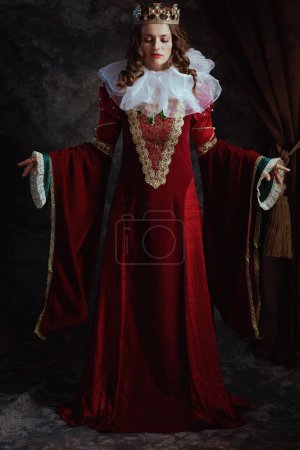 Foto de Retrato completo de la reina medieval en vestido rojo con cuello blanco y corona sobre fondo gris oscuro. - Imagen libre de derechos