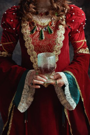 Téléchargez les photos : Gros plan sur la reine médiévale en robe rouge avec gobelet sur fond gris foncé. - en image libre de droit