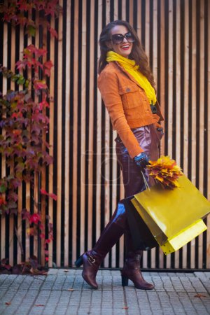 Photo for Hello autumn. Full length portrait of happy modern female in orange trench coat with shopping bags and autumn yellow leaves in the city. - Royalty Free Image