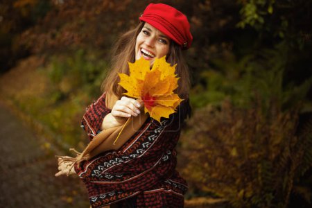Foto de Hola otoño. mujer de moda feliz en sombrero rojo con hojas de otoño y bufanda caminando en el parque de la ciudad. - Imagen libre de derechos