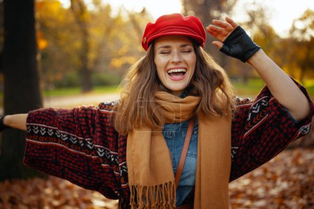 Foto de Hola otoño. sonriente joven hembra en sombrero rojo con bufanda y guantes en el parque de la ciudad. - Imagen libre de derechos
