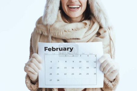 Photo for Happy modern 40 year old woman in winter coat and fur hat isolated on white in white gloves with february calendar. - Royalty Free Image