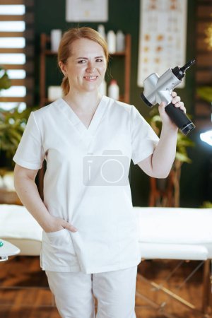 Photo for Healthcare time. happy female massage therapist in massage cabinet with massage pistol. - Royalty Free Image