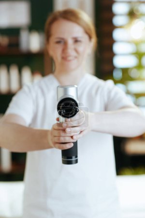 Photo for Healthcare time. Closeup on happy female massage therapist in massage cabinet with massage pistol. - Royalty Free Image