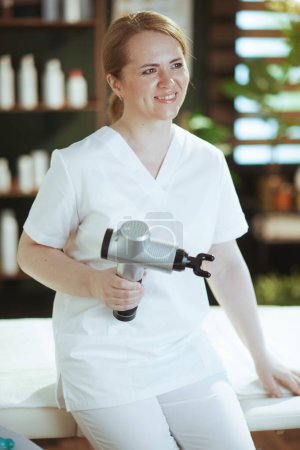 Photo for Healthcare time. smiling female massage therapist in spa salon with massage pistol. - Royalty Free Image