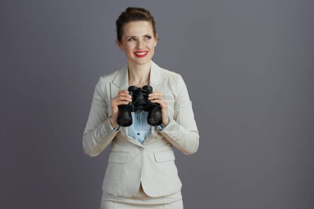 Téléchargez les photos : Heureuse jeune propriétaire de petite entreprise femme dans un costume d'affaires léger avec jumelles sur fond gris. - en image libre de droit