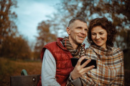 Foto de Hola otoño. sonriente pareja moderna en el parque con teléfono inteligente. - Imagen libre de derechos