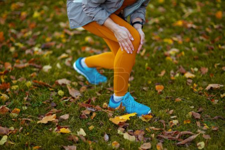 Téléchargez les photos : Bonjour l'automne. Gros plan sur la femme d'âge moyen en vêtements de fitness dans le parc a eu une blessure à la jambe. - en image libre de droit