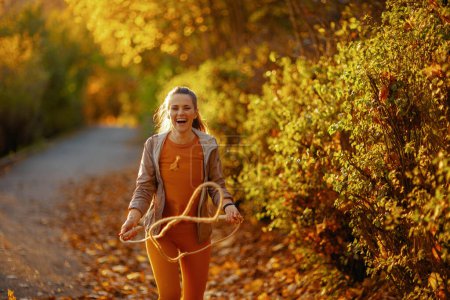 Photo for Hello autumn. smiling elegant woman in fitness clothes in the park with jump rope. - Royalty Free Image