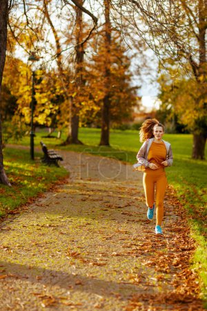 Photo for Hello autumn. trendy 40 years old woman in fitness clothes in the park running. - Royalty Free Image