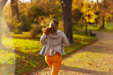 Téléchargez les photos : Bonjour l'automne. Vu de derrière femme moderne en vêtements de fitness dans le parc jogging. - en image libre de droit