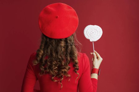 Photo for Happy Valentine. Seen from behind middle aged woman with candy on stick and long wavy hair isolated on red. - Royalty Free Image
