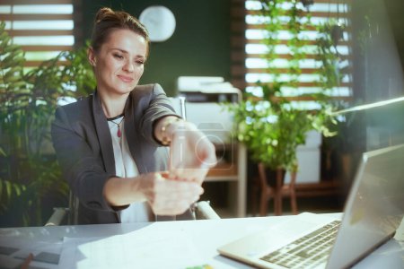 Foto de Lugar de trabajo sostenible. sonriente mujer de negocios moderna en la oficina verde moderna con el ordenador portátil que extiende las manos. - Imagen libre de derechos