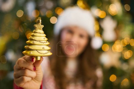 Foto de En Navidad. Primer plano de la mujer de mediana edad con sombrero de Santa que muestra el juguete de Navidad cerca del árbol de Navidad en la sala de estar. - Imagen libre de derechos