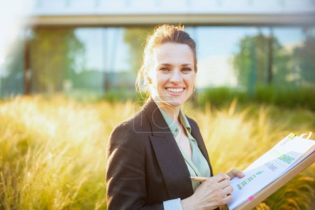 Photo for Smiling modern 40 years old woman employee near business center in black jacket with documents and folder. - Royalty Free Image