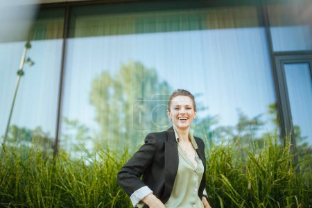 Téléchargez les photos : Travailleuse moderne souriante près du centre d'affaires en veste noire. - en image libre de droit