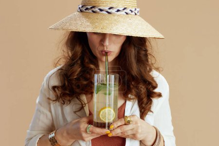 Téléchargez les photos : Vacances à la plage. femme au foyer tendance en chemisier blanc et short isolé sur fond beige avec cocktail et chapeau d'été. - en image libre de droit