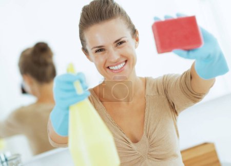 Photo for Happy young housewife showing spray bottle and sponge - Royalty Free Image