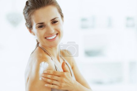 Foto de Sonriente mujer joven aplicando crema en el baño - Imagen libre de derechos