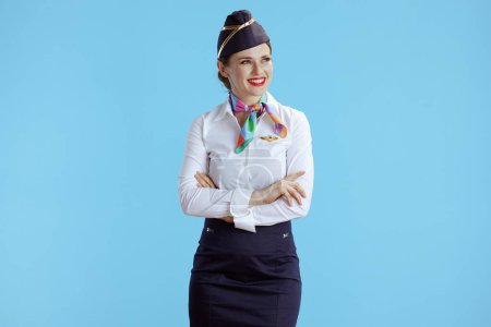 Téléchargez les photos : Heureuse élégante hôtesse de l'air femme sur fond bleu en uniforme regardant l'espace de copie. - en image libre de droit