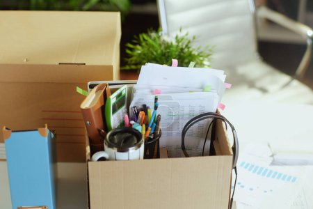 Photo for New job. table in modern green office with personal belongings in cardboard box. - Royalty Free Image