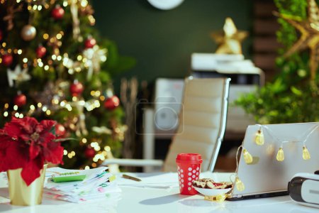 Foto de Moderna oficina verde decorada de Navidad con ordenador portátil, poinsettia, bebida de Navidad y galletas. - Imagen libre de derechos