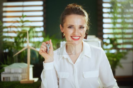 Photo for Eco real estate business. Portrait of smiling modern 40 years old woman realtor in modern green office in white blouse with keys. - Royalty Free Image