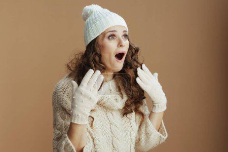 Foto de Hola invierno. mujer de mediana edad con estilo sorprendido en suéter beige, mitones y sombrero sobre fondo beige. - Imagen libre de derechos