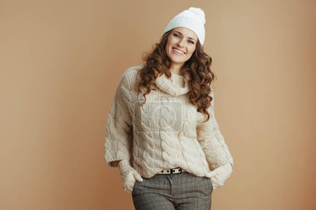 Téléchargez les photos : Bonjour l'hiver. Portrait de femme moderne souriante en pull beige, mitaines et chapeau isolés sur beige. - en image libre de droit