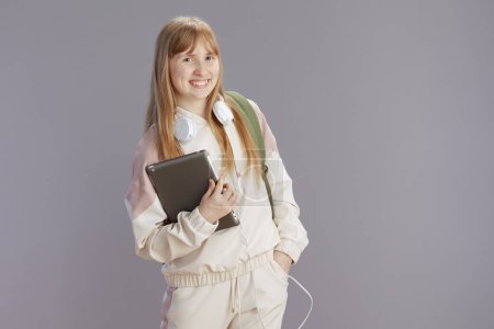 Téléchargez les photos : Portrait d "élève heureux à la mode en survêtement beige avec écouteurs et tablette numérique isolé sur gris. - en image libre de droit