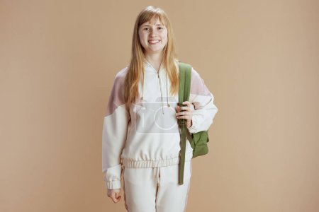 Foto de Retrato de chica adolescente de moda sonriente en chándal beige con mochila contra fondo beige. - Imagen libre de derechos