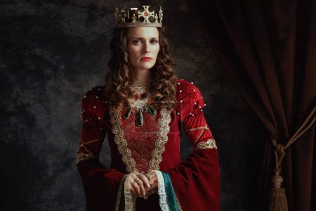 Photo for Medieval queen in red dress with crown on dark gray background. - Royalty Free Image