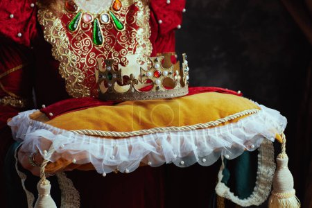 Téléchargez les photos : Gros plan sur la reine médiévale en robe rouge avec couronne sur oreiller sur fond gris foncé. - en image libre de droit