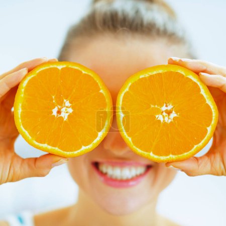 Photo for Happy young woman holding two slices of orange in front of eyes - Royalty Free Image